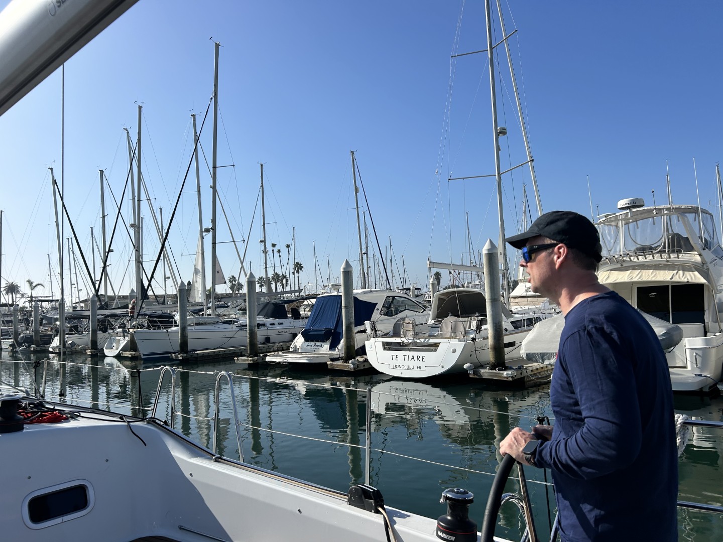 Sailor steering a sailboat through a marina surrounded by docked boats in San Diego.